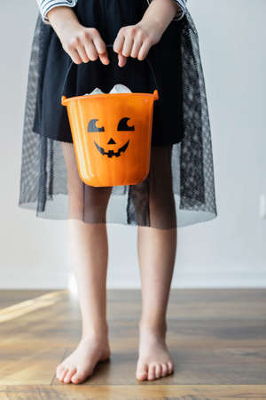 Halloween. A girl dressed as a witch is holding a pumpkin bucket full of sweets. Ideal for holiday illustrations. Trick or treatの写真素材