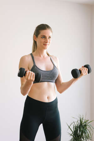 Young beautiful girl is engaged with dumbbells at home.の写真素材