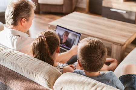 Video call using laptop from home. Dad and children sit on the couch and call mom online. Communication at a distanceの写真素材