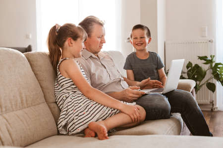 Vido call. Dad and children sit on the couch and call online grandparents or mom. Communication online, at a distance using the Internet.の写真素材