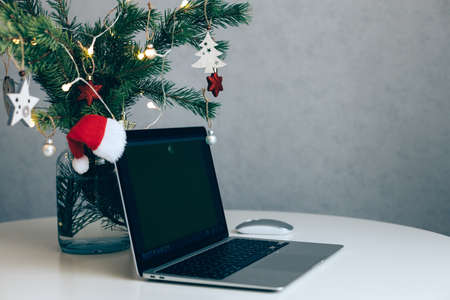 An open laptop on the table next to a Christmas tree decorated with balls and a garland. New Year and Christmas mood in the workplaceの写真素材