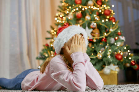 A cute girl lies by the Christmas tree and dreams. Dreams Come True. Children waiting for the new year and christmasの写真素材