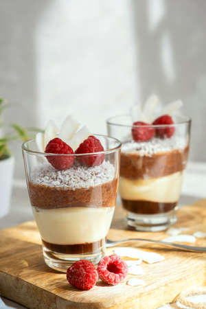 Three-layer mousse dessert made of chocolate and vanilla, decorated with fresh raspberries and coconut flakes in glasses on the table. Brunch, dessert for lovers.の写真素材
