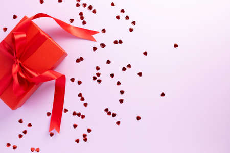 Red gift box decorated with a red ribbon on a pink background with sparkles in the form of a heart. Gifts for loved ones. Flat layの写真素材