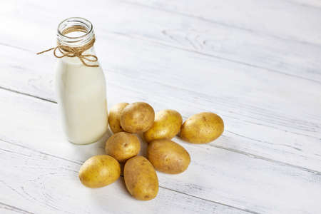 Potato milk in a glass bottle is on the table next to potato tubers. Alternative, vegetable milk is ideal for vegans. Food trends. Copy spaceの写真素材