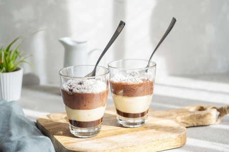 Three-layer chocolate and vanilla mousse dessert in glass cups, sprinkled with coconut flakes, on a...