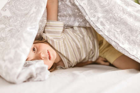 An adorable boy, Toddler, plays on the parents bed. Sits wrapped in a blanket and laughs. Family funの写真素材