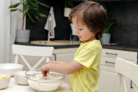 The boy prepares dough for biscuit or baking in the kitchen. The kid mixes the ingredients with a...