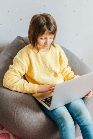 A girl sits in her room with a laptop on her lap and watches lessons or training courses. Children...