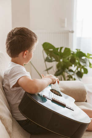 Adorable little boy learning to play acoustic guitar at home. Hobbies and entertainment for children at homeの写真素材