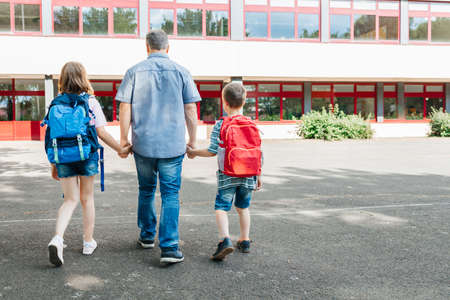 A young dad leads his children by the hand with backpacks on their backs to school. Back to school....