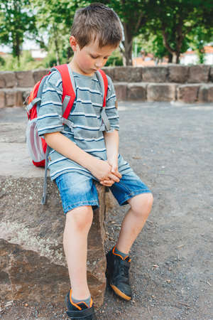 A sad schoolboy sits in the school yard with a backpack on his back. Childrens problems at school....