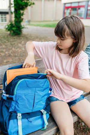 A teenage girl sits in the school yard and takes textbooks out of her backpack
