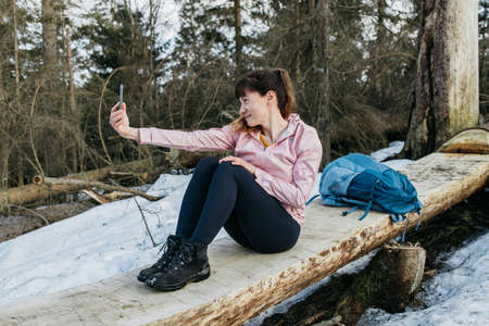 A cute young woman is using a mobile phone while on vacation in the forest. The traveler is talking...