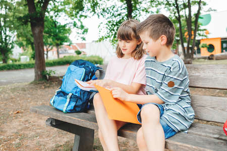 Schoolchildren sit at recess from lessons in the school yard and look at the textbook. Sister helps...