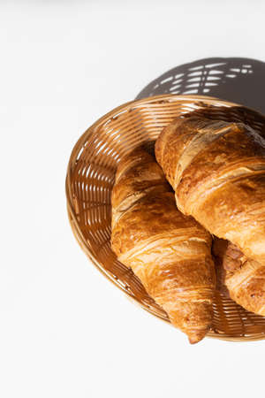 Fresh croissants in a wicker basket in the bright rays of the sun. Fresh pastries for breakfast. Home baking, bakery.の写真素材