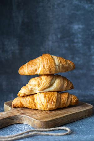 Fresh croissants lie on a cutting board on a dark background. Home baking, bakery
