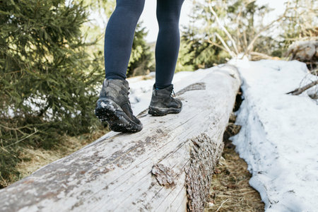 Close-up of the legs of a girl in trekking boots walking on a log in the forest