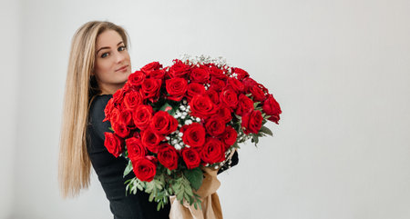 Charming young woman with a huge bouquet of red roses. Gift for birthday or valentines day. Engagement and signs of loveの写真素材