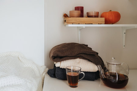 A stack of autumn sweaters next to warm tea and candles. Autumn moodの写真素材