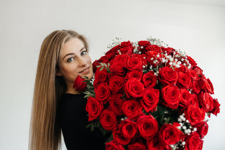 Charming girl with a huge bouquet of scarlet roses. The girl is happy with a gift from her belovedの写真素材