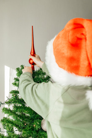 New Years and Christmas. Children are waiting for the holiday. Child boy in a santa claus hat decorates the Christmas tree with New Years toys.の写真素材
