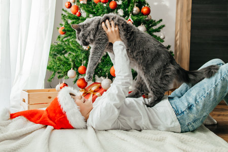 Portrait of a happy teenage girl and her gray maine coon cat next to a decorated Christmas tree. Friendship with petsの写真素材