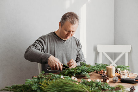 A man at home makes a Christmas wreath from fresh spruce branches. Decorating your home for the holidays.の写真素材