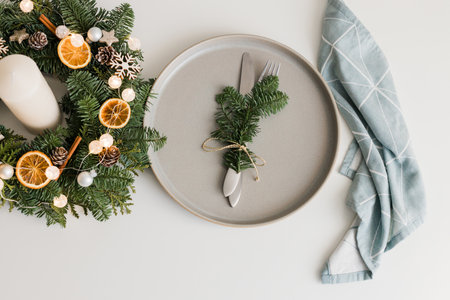 Christmas or New Year table setting with ceramic plate, fir branch with decor and cutlery. View from...