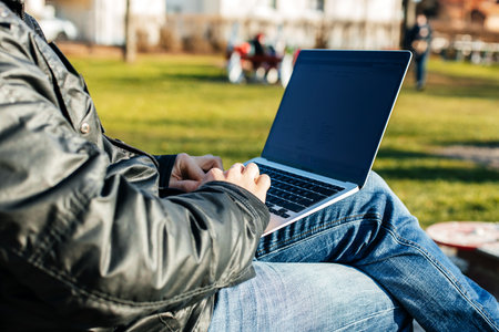 Close-up of the hands of a man working on a laptop on the street, sitting on a bench. Remote work conceptの写真素材