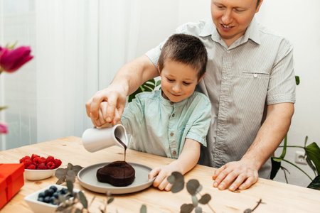 Dad and son are preparing a congratulatory cake, pouring chocolate icing on the cake. Mothers Day, International Womens Day, Valentines Day.の写真素材