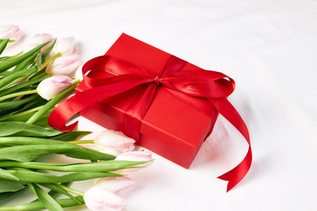 A bouquet of pink tulips and a red gift box on a beige bedspread. Gifts for the holidays. valentines...