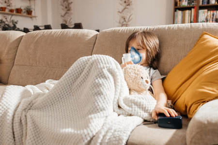 Little boy makes inhalation with a nebulizer at home lying on the couch. Cough prevention and treatment at homeの写真素材