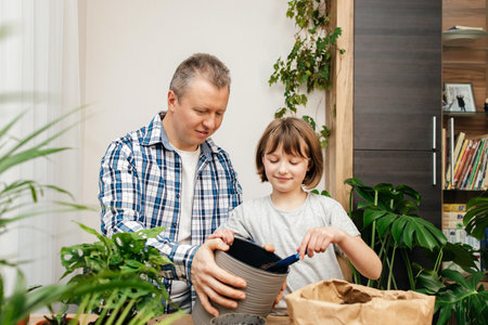 A teenage girl helps her dad to transplant a monstera houseplant into another pot. Transplantation and care of indoor flowers. home gardening.の写真素材