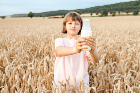 Happy teen girl holding a bottle of fresh milk while standing in a cereal field. The concept of healthy food and organic productsの写真素材