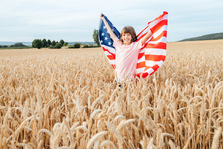 Happy girl with american flag in wheat field. Freedom and patriotism of children. Independence Day 4th of Julyの写真素材