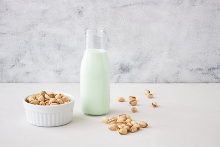 Pistachio milk in a bottle on a gray table next to pistachios. Vegetable milk. Nut milk for vegansの写真素材