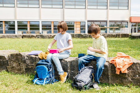 Children sit on in the school yard and eat apples and sandwiches. Snack during break time during classの写真素材