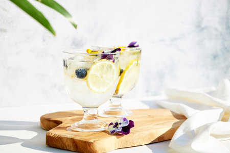 Chilled cocktails with fresh citrus fruits garnished with edible flowers on a wooden serving board....