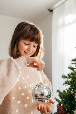 A teenage girl decorates a Christmas tree with a ball-shaped toy. Waiting and preparing for the holidayの写真素材