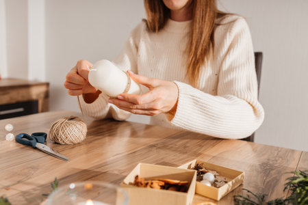 Close-up of a girls hands decorating candles with New Year or Christmas decor. Woman creates holiday decorations, candles for home.の写真素材