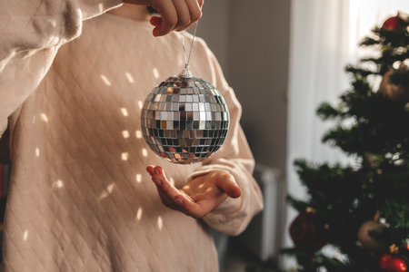 Close-up of the hands of a girl holding a disco ball against the background of a decorated Christmas tree. Celebration atmosphereの写真素材