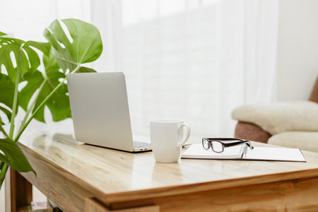 The laptop is on the table next to glasses, a notepad and a cup of coffee. A workspace at home. Distant workの写真素材