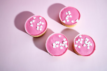 Pink cupcakes with frosting and heart shaped sprinkles on a pink backgroundの写真素材