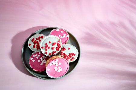 Sponge cake cupcakes with icing decorated with sugar sprinkles in the shape of hearts on a plate on...