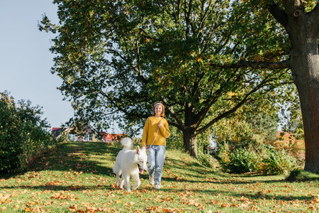 Teenage girl walking her dog, a white Swiss shepherd, outside on a sunny autumn day.の写真素材