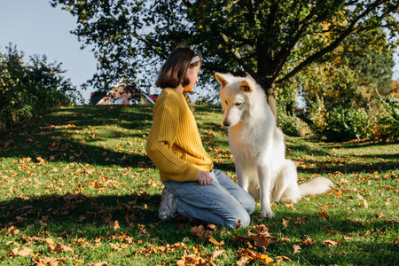 Teenage girl spending time with her dog white swiss shepherd outside. Girl playing with dog