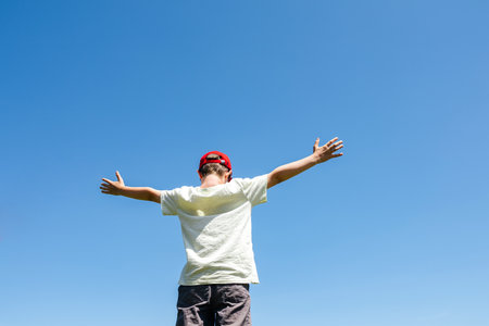 Boy wearing red cap raising arms to the skyの写真素材