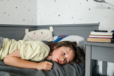 Young boy lying in bed looking thoughtfulの写真素材