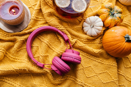 Pink headphones, candles, pumpkins, and tea on a cozy blanket